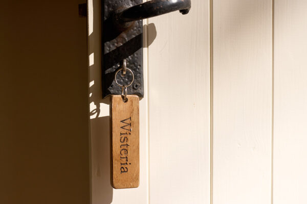 a door key in keyhole with wooden key ring with the name of the holiday cottage 'Wisteria' etched into the wood.